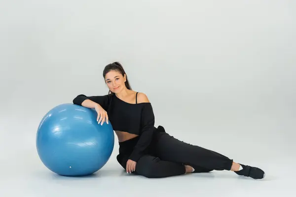 Fit female athlete relaxes by a blue exercise ball in studio lighting. — Stock Photo