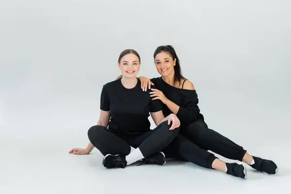 Two strong women wearing matching fitness attire enjoy a moment of friendship indoors. — Stock Photo