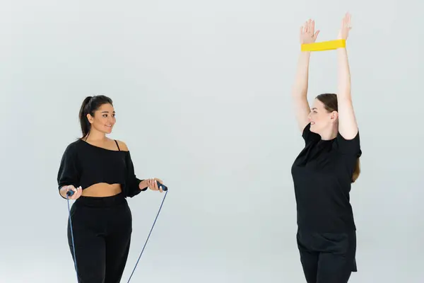Two fit females participate in a dynamic exercise session using resistance bands and jump ropes. — Stock Photo