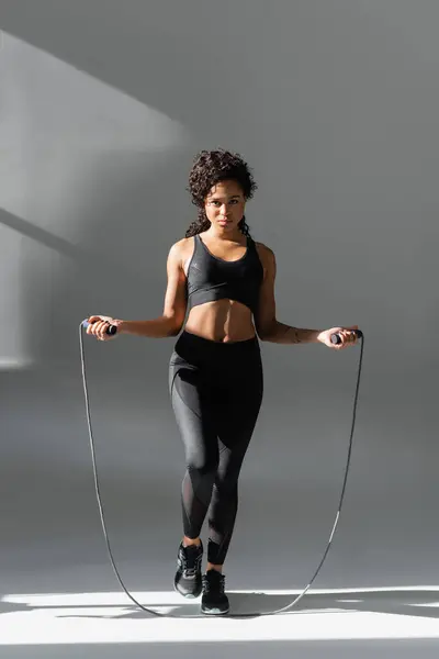 A confident woman engages in an energetic jump rope workout while showcasing her fitness and style. — Stock Photo