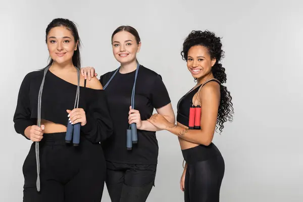 Three fit women hold jump ropes while dressed in matching black sportswear, smiling confidently. — Stock Photo