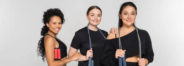 Three fit women smile while jumping rope, showcasing friendship in trendy activewear. — Stock Photo