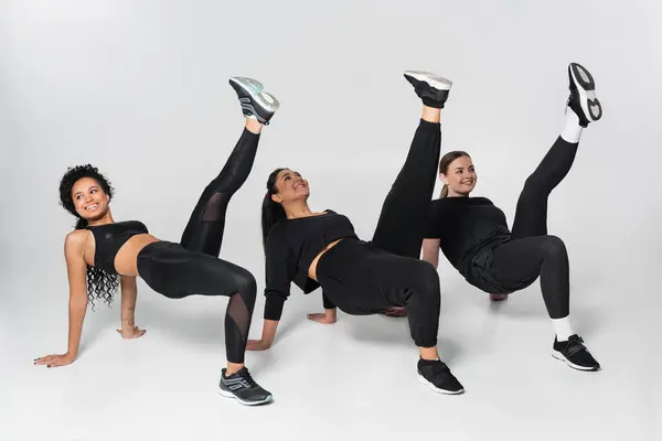 Três mulheres aptas mostram força e elegância em trajes esportivos enquanto fazem exercícios dinâmicos. — Fotografia de Stock