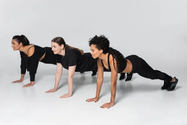 Three fit women engage in synchronized push ups, showcasing strength and teamwork indoors. — Stock Photo