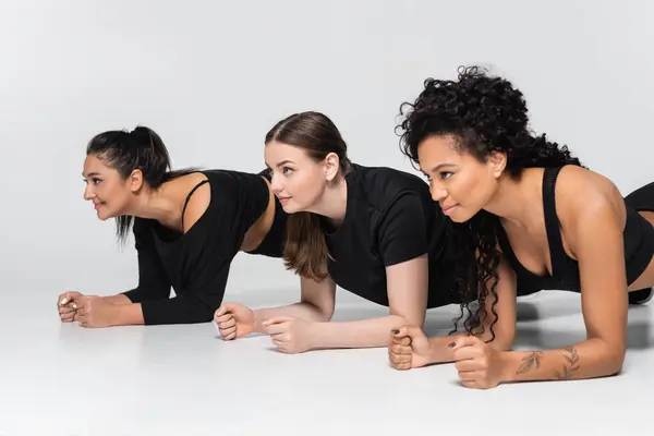 Tres mujeres participan en un ejercicio desafiante tablón de fitness, demostrando fuerza y unidad. - foto de stock
