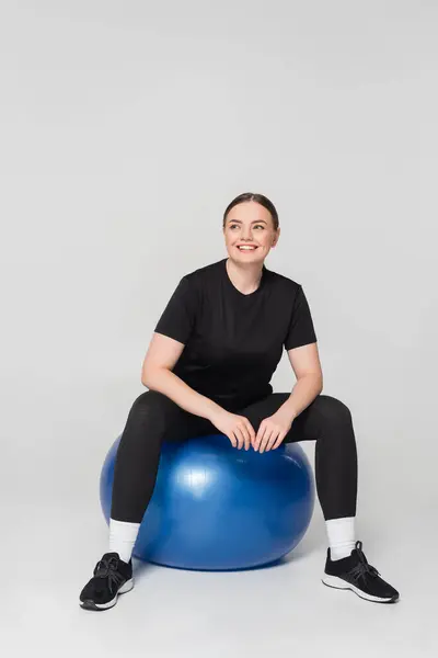 Fit woman smiles while balancing on a stability ball in athletic wear, showing her strength. — Stock Photo