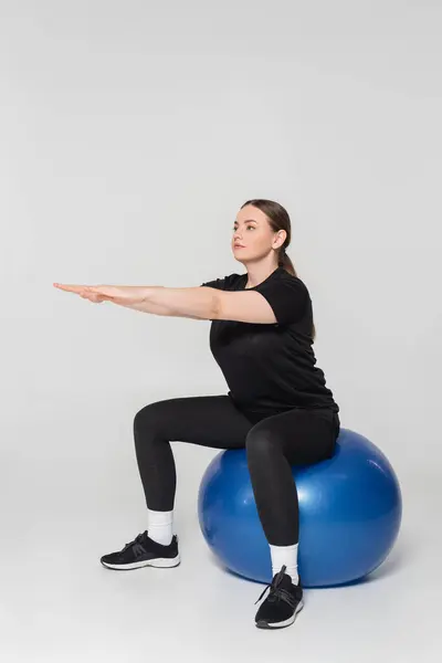 Mulher forte se concentra em sua rotina de treino, enquanto se equilibra em uma bola de estabilidade em casa. — Fotografia de Stock