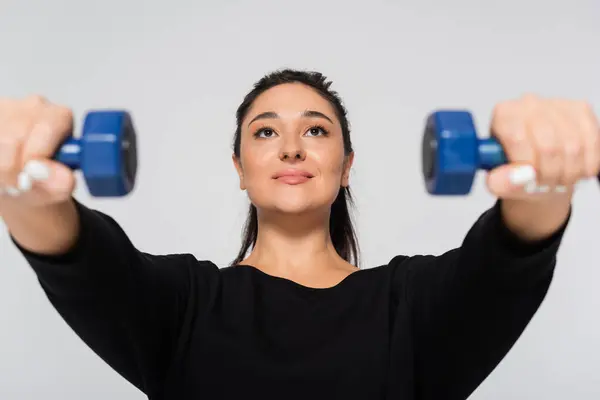 A fit female enthusiast showcases her strength while lifting dumbbells in an indoor space. — Stock Photo