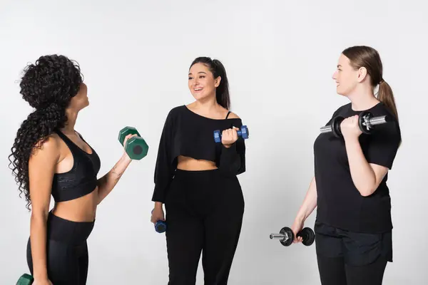 Tres mujeres fuertes comparten consejos de acondicionamiento físico mientras levantan pesas, construyendo una comunidad de apoyo. - foto de stock