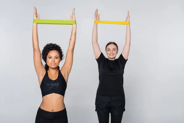 Two fit women showcase strength through resistance band exercises in a bright setting. — Stock Photo
