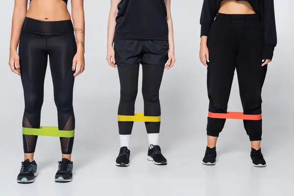 Three women showcase their strength and fitness by using resistance bands in stylish active wear. — Stock Photo