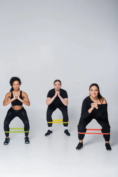 Three women engage in leg exercises using resistance bands, showcasing teamwork and strength. — Stock Photo