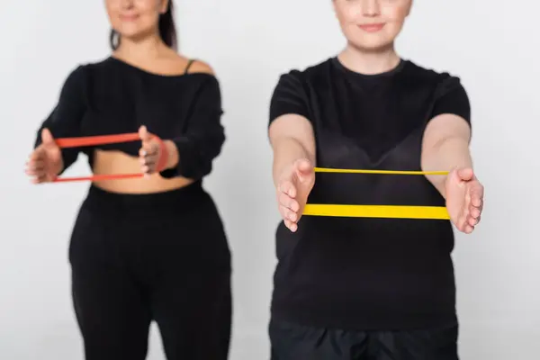 Two fit women perform strength training exercises with colorful resistance bands in a bright studio. — Stock Photo
