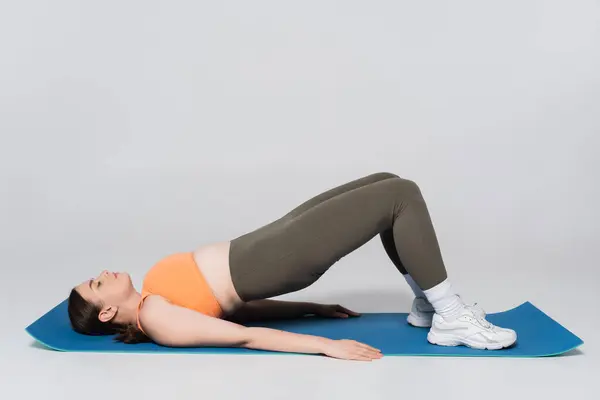 A strong woman performs a bridge exercise on a blue mat, showcasing fitness and strength. — Stock Photo