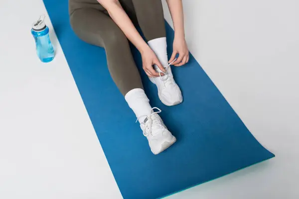 A determined woman ties her shoes on a yoga mat, focused on her upcoming fitness routine. — Stock Photo