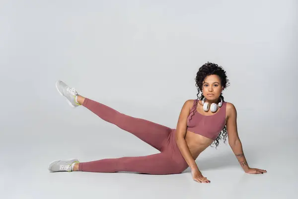 Donna forte e in forma esegue una routine di allenamento mentre indossa abbigliamento sportivo elegante e cuffie. — Foto stock