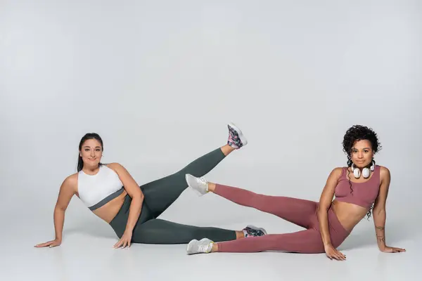 Two fit women perform leg lifts in workout attire, showcasing strength and determination together. — Stock Photo