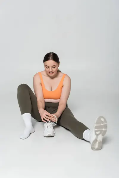 A fit woman sits on the floor tying her sneakers, focused and ready to elevate her fitness game. — Stock Photo