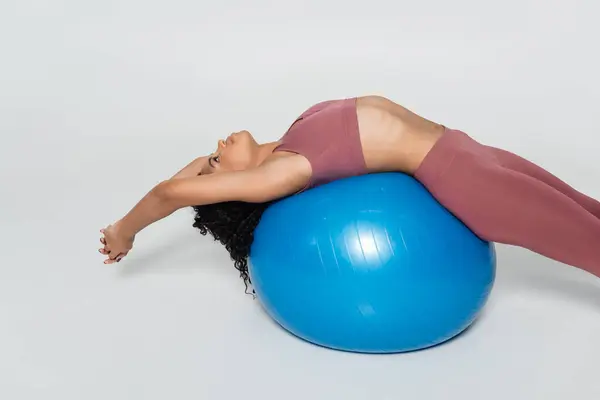 A female athlete performs a stretching exercise on a blue stability ball in a modern fitness studio. — Stock Photo