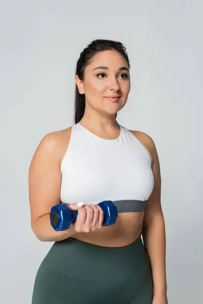 Selbstbewusste Frau hält eine Hantel in der Hand, während sie Kraft und Fitness in einem minimalistischen Raum verkörpert. — Stockfoto