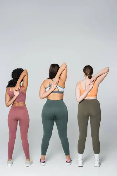 Three fit women in vibrant sportswear stretch their arms, showcasing strength. — Stock Photo