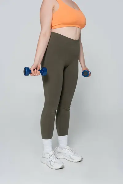 A strong woman engages in a workout, holding dumbbells while showcasing her fit physique. — Stock Photo