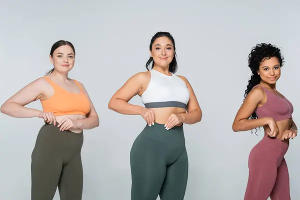 Three strong and fit women highlight their vibrant sportswear while posing confidently together. — Stock Photo