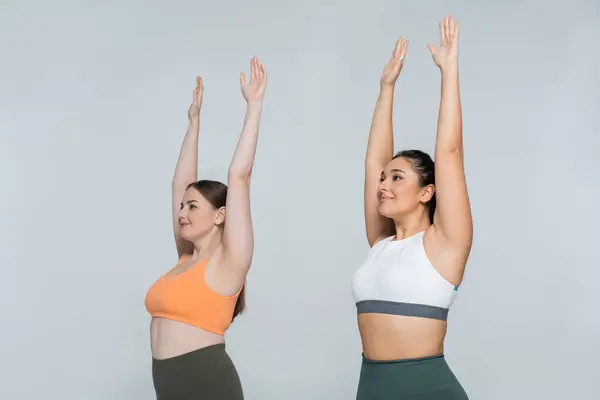 Two fit women express joy and strength while stretching upwards in stylish activewear. — Stock Photo