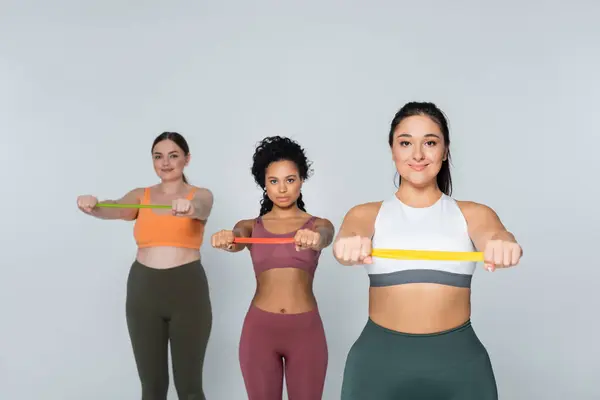 Tres mujeres fuertes realizan ejercicios de banda de resistencia mostrando su físico en forma y confianza. - foto de stock