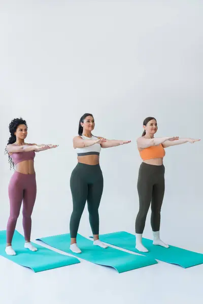 Three strong women practice synchronized fitness poses on vibrant mats in a well lit studio space. — Stock Photo