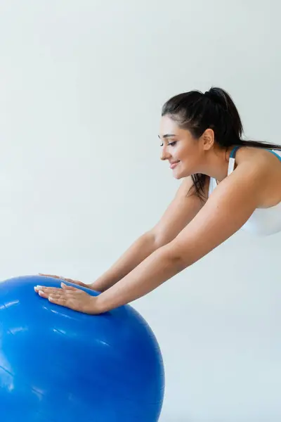 Strong and fit woman is focused on her workout with a blue stability ball in a bright space. — Stock Photo
