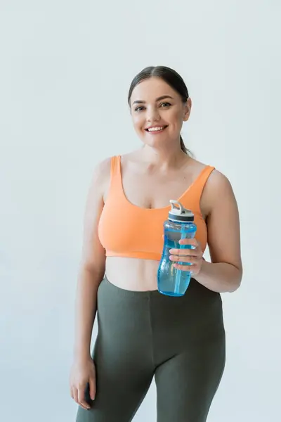 Una mujer en forma posa con confianza con una botella de agua azul, lista para su entrenamiento. - foto de stock