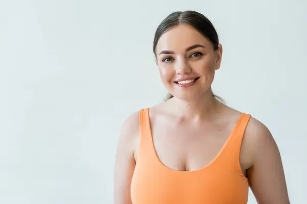 Una donna in forma sorride brillantemente mentre indossa abbigliamento sportivo luminoso, irradiando forza e positività.. — Foto stock
