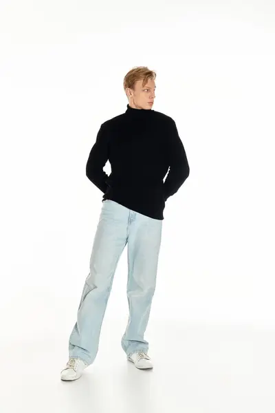 Um jovem elegante em uma camisola preta e jeans leves fica alto e charmoso. — Fotografia de Stock