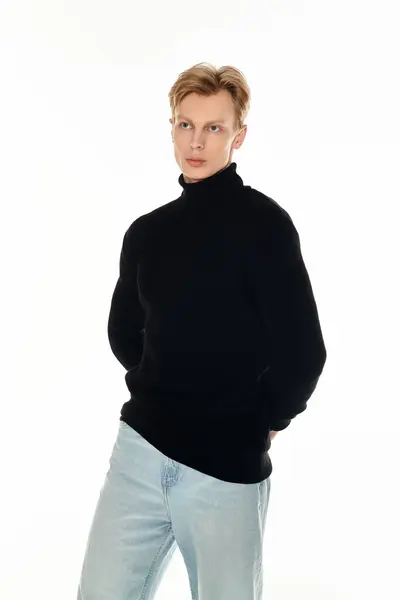 Ein junger Mann präsentiert seinen Charme in einem schicken schwarzen Pullover und hellen Jeans, der Zuversicht ausstrahlt. — Stockfoto