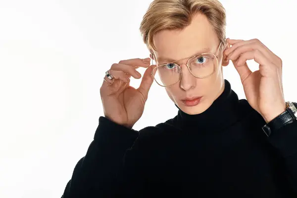 Stylish young man adjusts his glasses, showcasing a confident expression within a bright studio. — Stock Photo