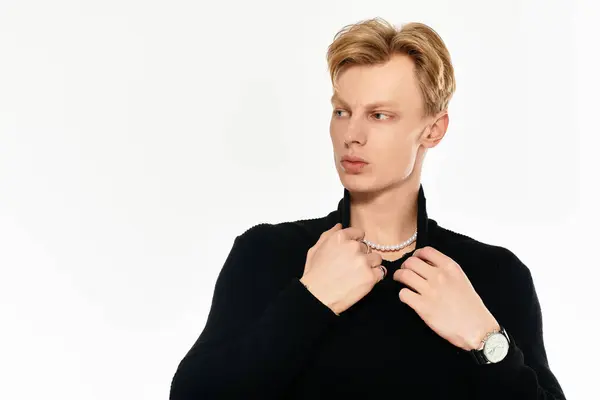 Confident young man in a dark sweater adjusts accessories in a minimalist space. — Stock Photo