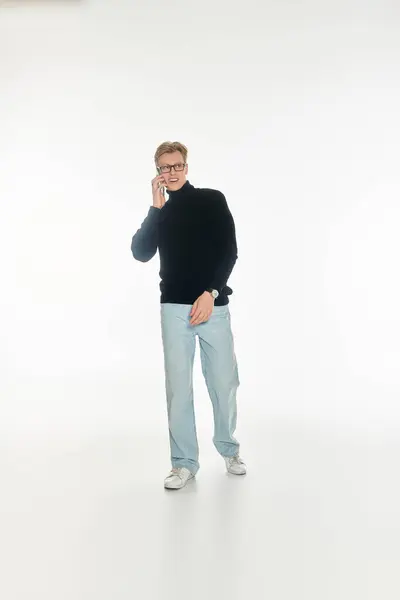 Un joven se pone de pie con confianza, hablando por teléfono en un entorno brillante y mínimo. - foto de stock