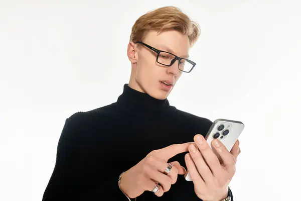 Um jovem elegante vestido de preto verifica seu smartphone com concentração e interesse. — Fotografia de Stock