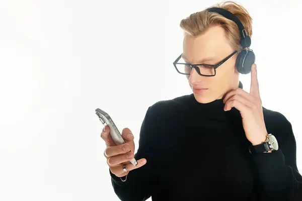 A young handsome man listens to music through headphones while intently browsing his phone. — Stock Photo