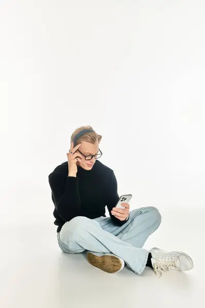 Thoughtful young man engaged with his smartphone in a bright, minimalist setting. — Stock Photo