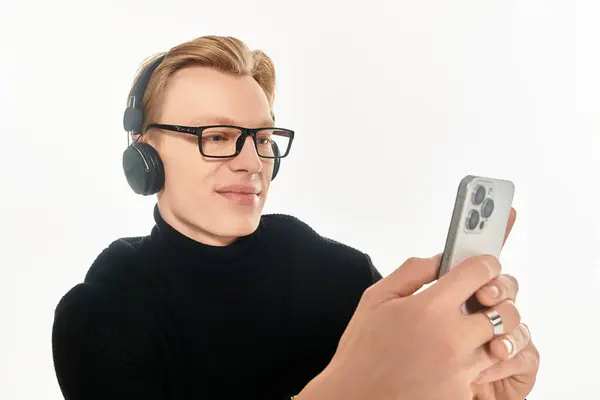 Smiling young man with glasses listens to music while focused on his smartphone display. — Stock Photo