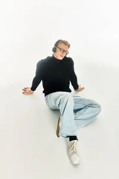 A young handsome man with glasses listens to music, lost in thought on a white surface. — Stock Photo