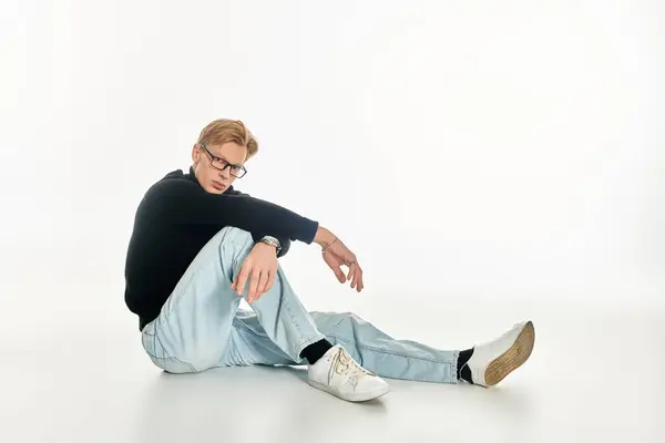 A stylish young man in trendy attire sits on the floor, projecting confidence and charm. — Stock Photo