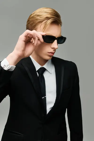 Junger gutaussehender Mann im scharfen Anzug stylt seine Sonnenbrille selbstbewusst drinnen. — Stockfoto