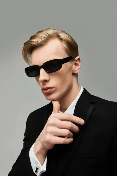 Jeune homme confiant pose élégamment dans un costume noir sur mesure et des lunettes de soleil, exsudant charme. — Photo de stock