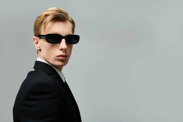Харизматичний молодий чоловік в костюмі і сонцезахисних окулярах виділяється на тлі нейтрального фону. — Stock Photo