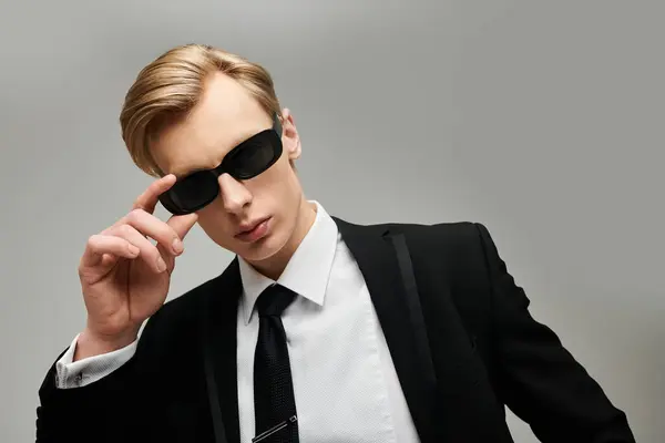 Ein junger Mann im schnittigen Anzug passt bei einer stilvollen Veranstaltung selbstbewusst seine Sonnenbrille an. — Stockfoto