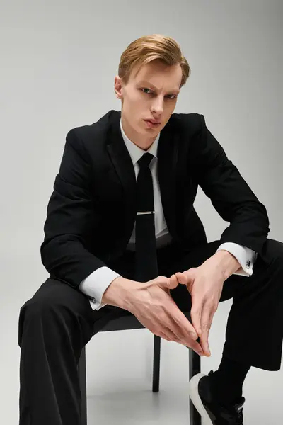 Confident young man in a sleek black suit showcases a polished look in a minimalist studio. — Stock Photo