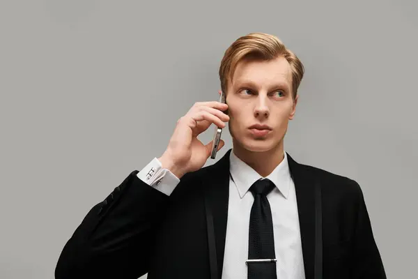 Stylish young man in a suit speaking on his phone with a serious expression in a muted background. — Stock Photo